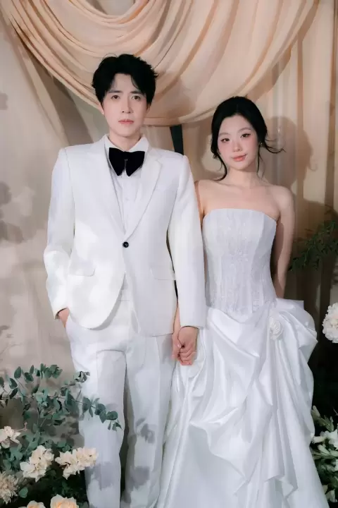Ảnh cưới Sài Gòn phong cách Hàn Quốc: cô dâu váy trắng đứng cạnh chú rể áo trắng trước rèm kem và hoa