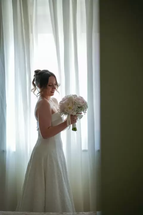 Ảnh cưới Sài Gòn phong cách Hàn Quốc: cô dâu cười, ôm bó hoa trắng bên rèm cửa sổ