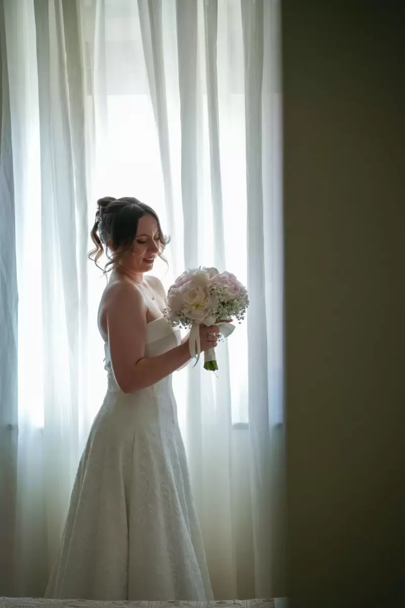 Ảnh cưới Sài Gòn phong cách Hàn Quốc: cô dâu cười, ôm bó hoa trắng bên rèm cửa sổ