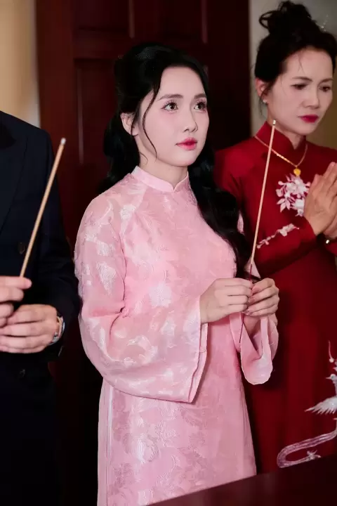Ảnh cưới Ninh Bình phong cách Phóng sự: cô dâu áo dài hồng cầm bó hoa, đứng giữa người thân