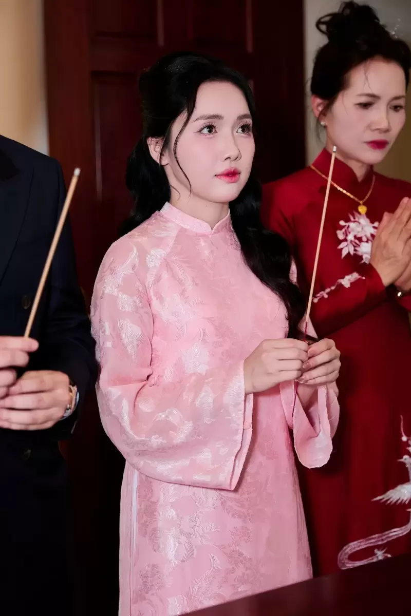 Ảnh cưới Ninh Bình phong cách Phóng sự: cô dâu áo dài hồng cầm bó hoa, đứng giữa người thân