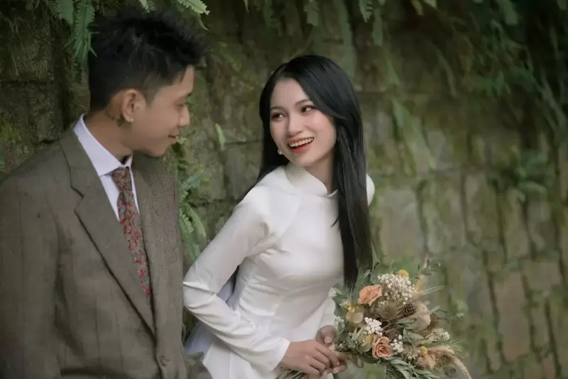 Áo dài gấm Thu Đông – váy cưới và trang phục cưới tại NHÂN DUYÊN: cô dâu áo dài trắng cầm bó hoa, cạnh chú rể