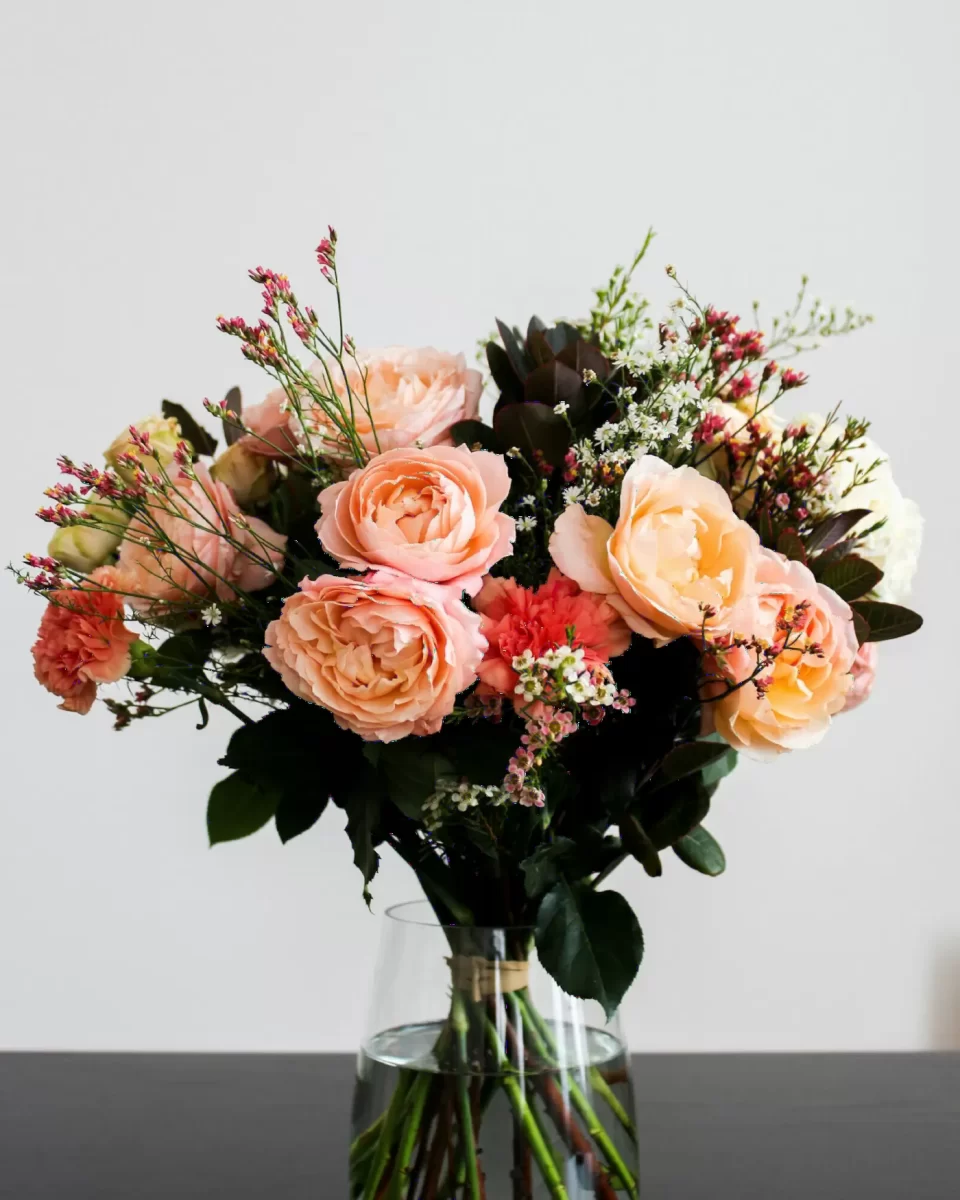 Bình hoa hồng đào cắm trong bình thủy tinh đặt trên nền xám, bìa số báo tuần này của PETAL & POST