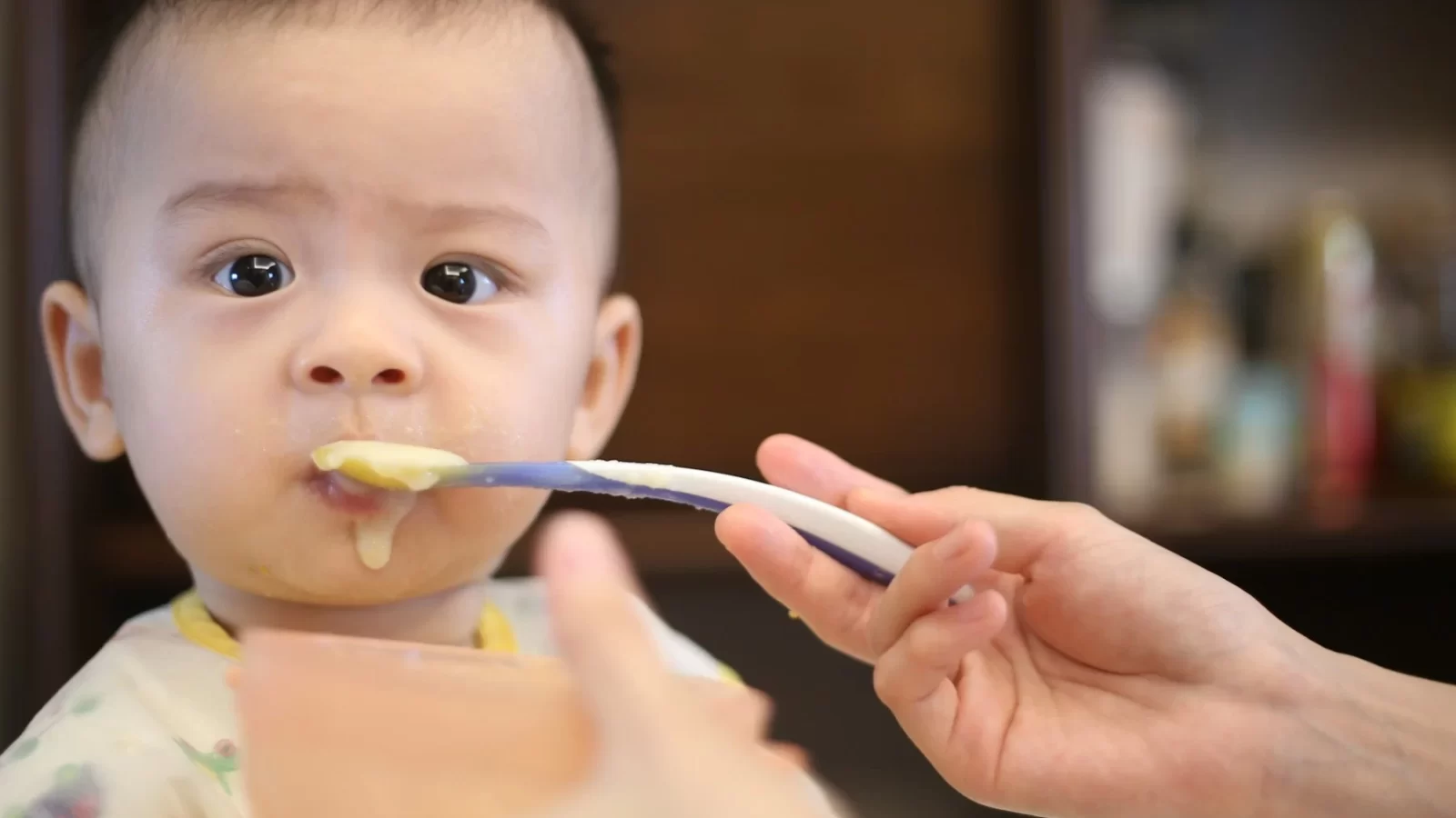 Bé nhỏ đang được mẹ đút ăn dặm bằng chiếc thìa nhỏ
