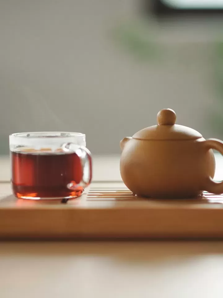 Chén trà thảo mộc màu hổ phách bên ấm đất nung trên khay gỗ