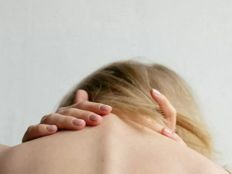 Người phụ nữ ngồi bên bàn làm việc, nghiêng đầu sang một bên để giãn cơ cổ
