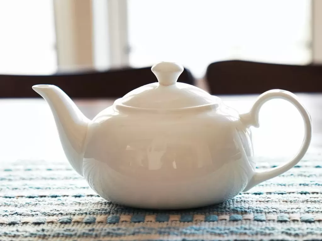Ấm trà sứ trắng trên khăn trải bàn đan