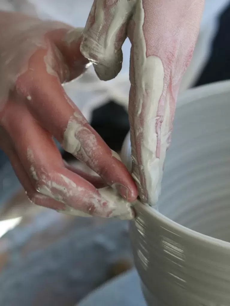 Đôi tay nghệ nhân đang vuốt miệng bình gốm trên bàn xoay