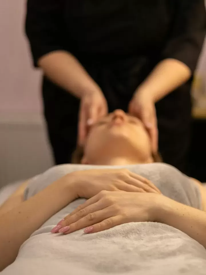 Kỹ thuật viên massage nhẹ vùng mặt và thái dương cho khách nằm thư giãn