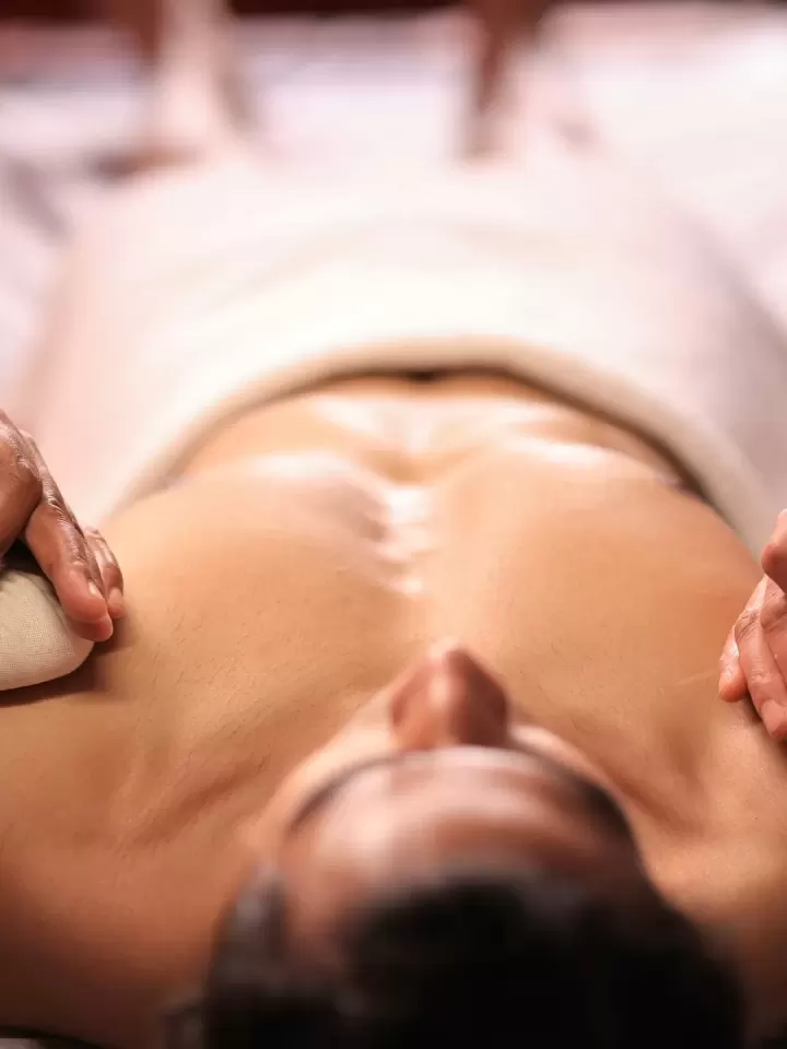 Kỹ thuật viên dùng hai túi chườm thảo dược ấn nhẹ dọc lưng khách