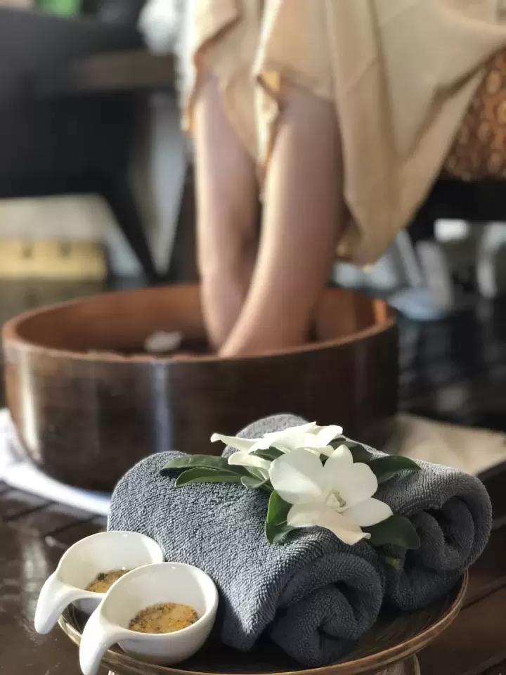 Đôi chân ngâm trong chậu gỗ nước thảo dược, khăn và hoa đặt bên cạnh