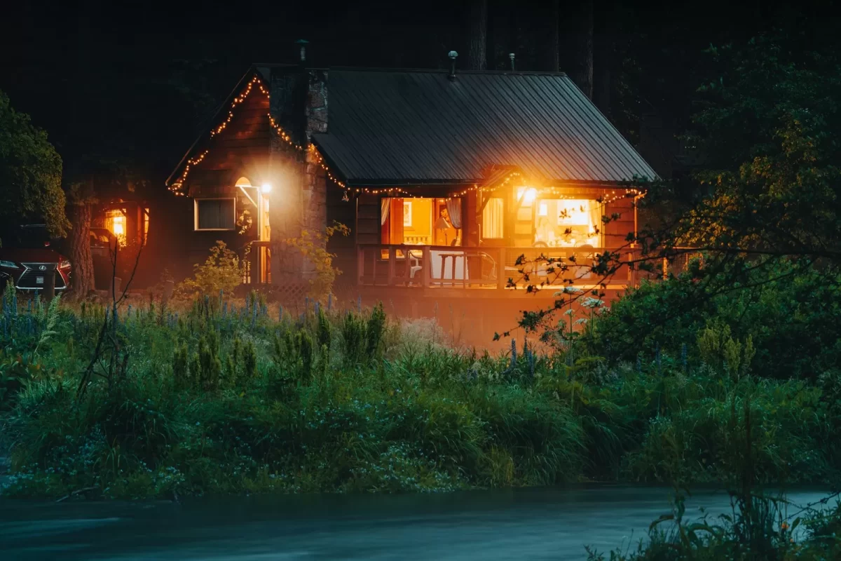 Cabin gỗ sáng đèn vàng giữa cỏ cây trong đêm