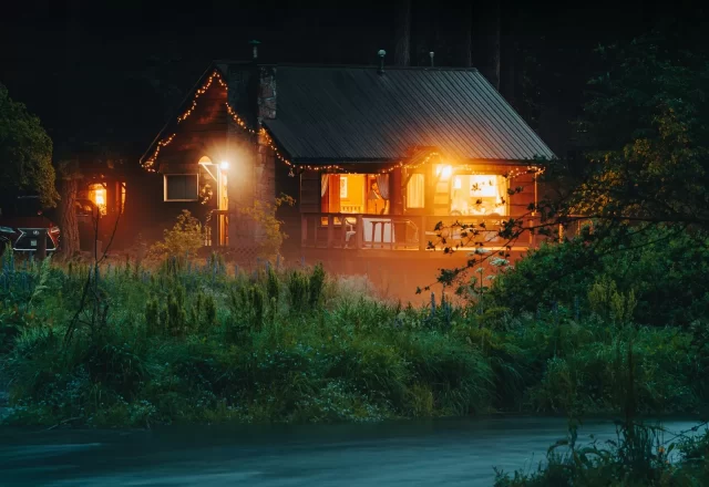 Cabin gỗ sáng đèn vàng giữa cỏ cây trong đêm