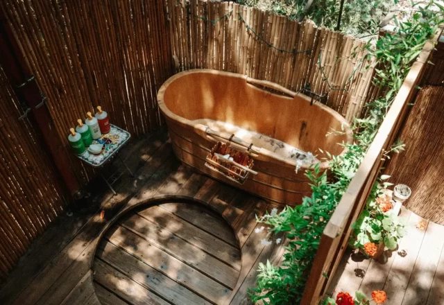 Bồn tắm gỗ ngoài trời bên hàng rào tre và cây xanh