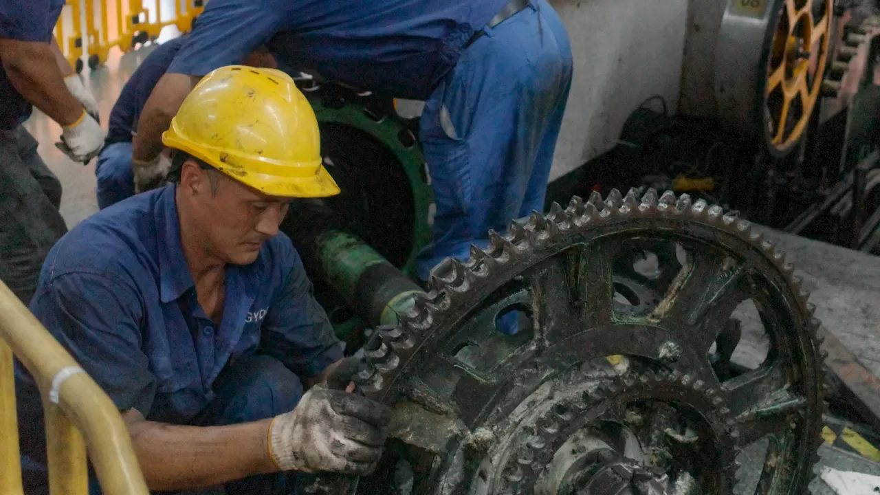 Công nhân đội mũ bảo hộ sửa cụm bánh răng máy công nghiệp