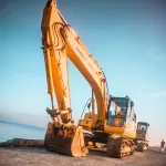 Máy đào bánh xích màu vàng trên nền đá cạnh mặt nước