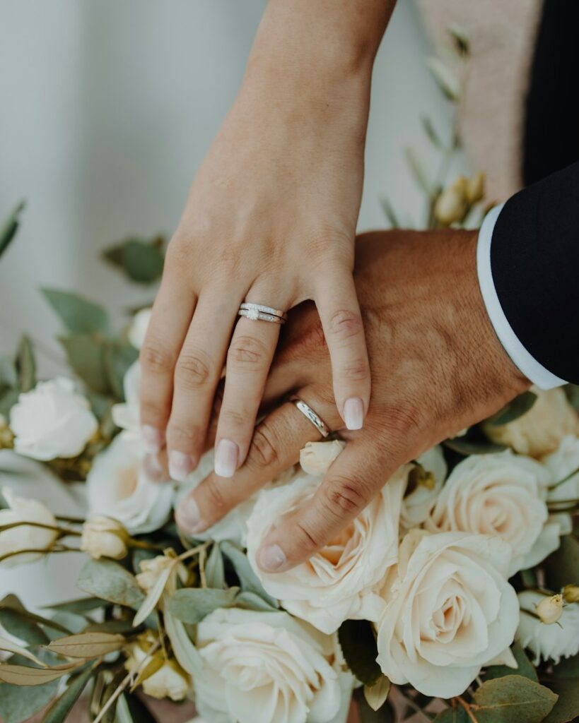 Đôi tay cô dâu chú rể với nhẫn cưới trên bó hoa