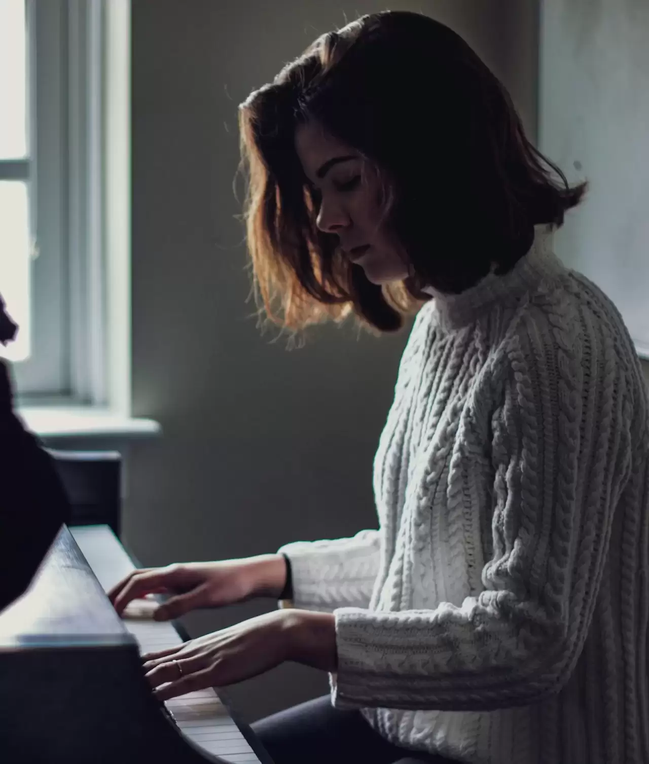Nữ nghệ sĩ tóc ngắn cúi đầu chơi piano bên cửa sổ