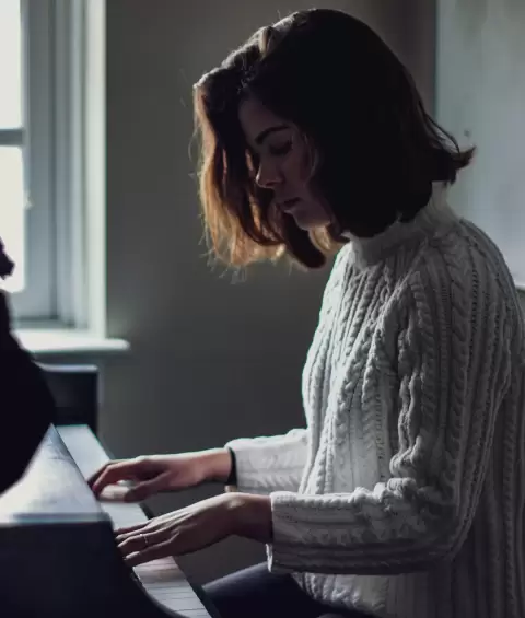 Nữ nghệ sĩ tóc ngắn cúi đầu chơi piano bên cửa sổ