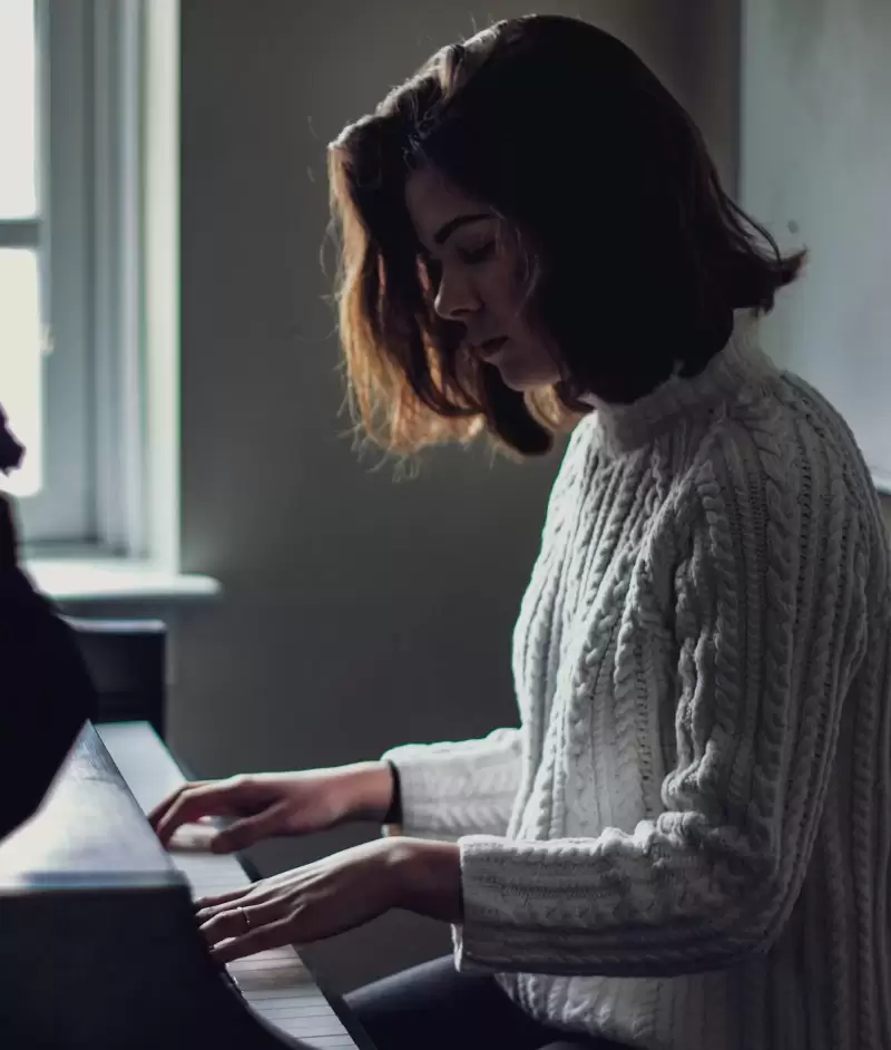 Nữ nghệ sĩ tóc ngắn cúi đầu chơi piano bên cửa sổ