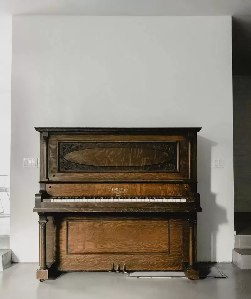 Cây đàn piano đứng bằng gỗ ấm cạnh bức tường trắng