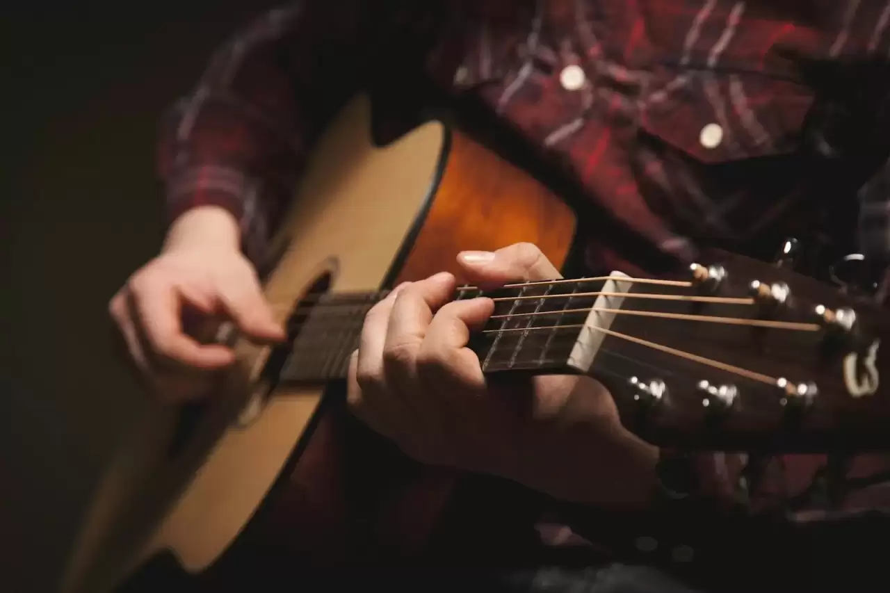 Người ngồi chơi guitar acoustic gỗ nâu