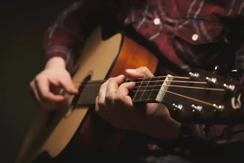 Người ngồi chơi guitar acoustic gỗ nâu